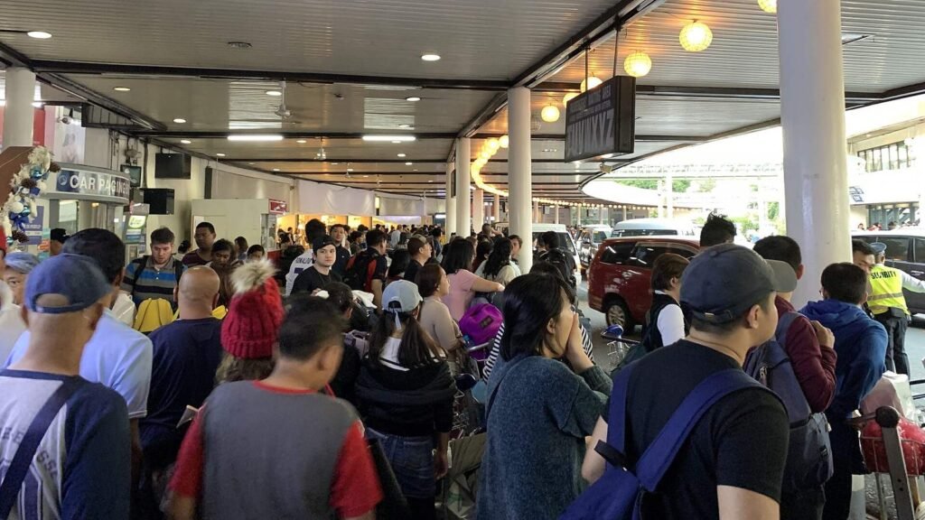 Crowd with luggage carts under paper lanterns at the NAIA arrivals curb on 23 December 2019
